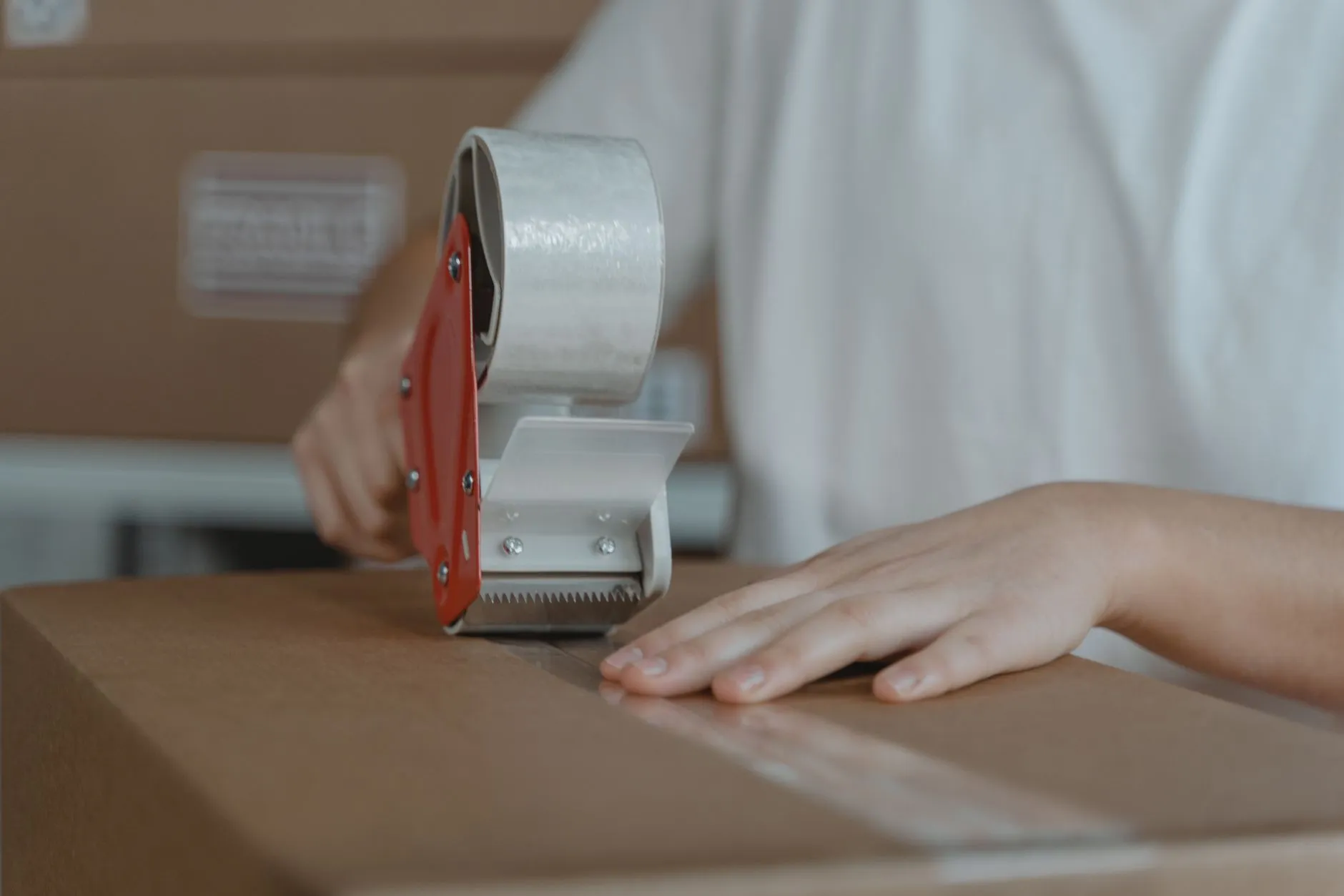 Hands sealing a cardboard parcel with a tape gun, packing an online store order