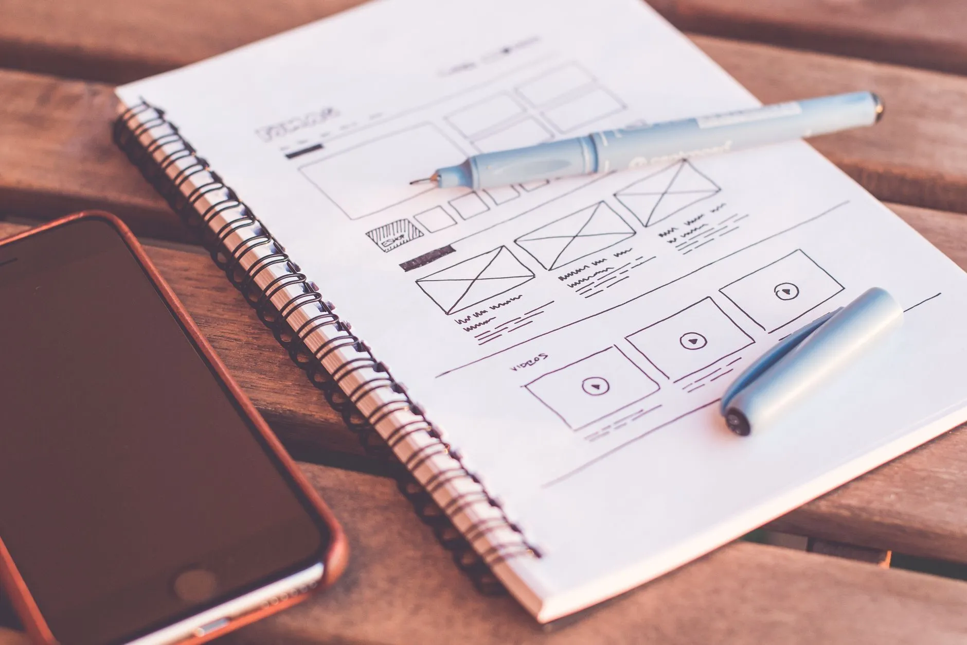 Notebook with website wireframe sketches and a smartphone on a wooden desk