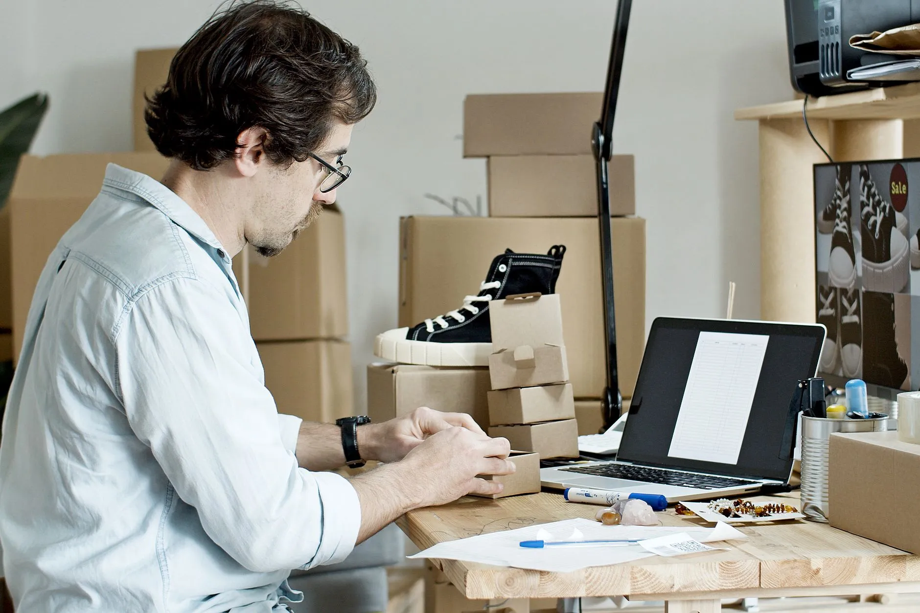 Store owner packing small boxes beside a laptop with an order list open, the kind of online store ecommerce SEO serves