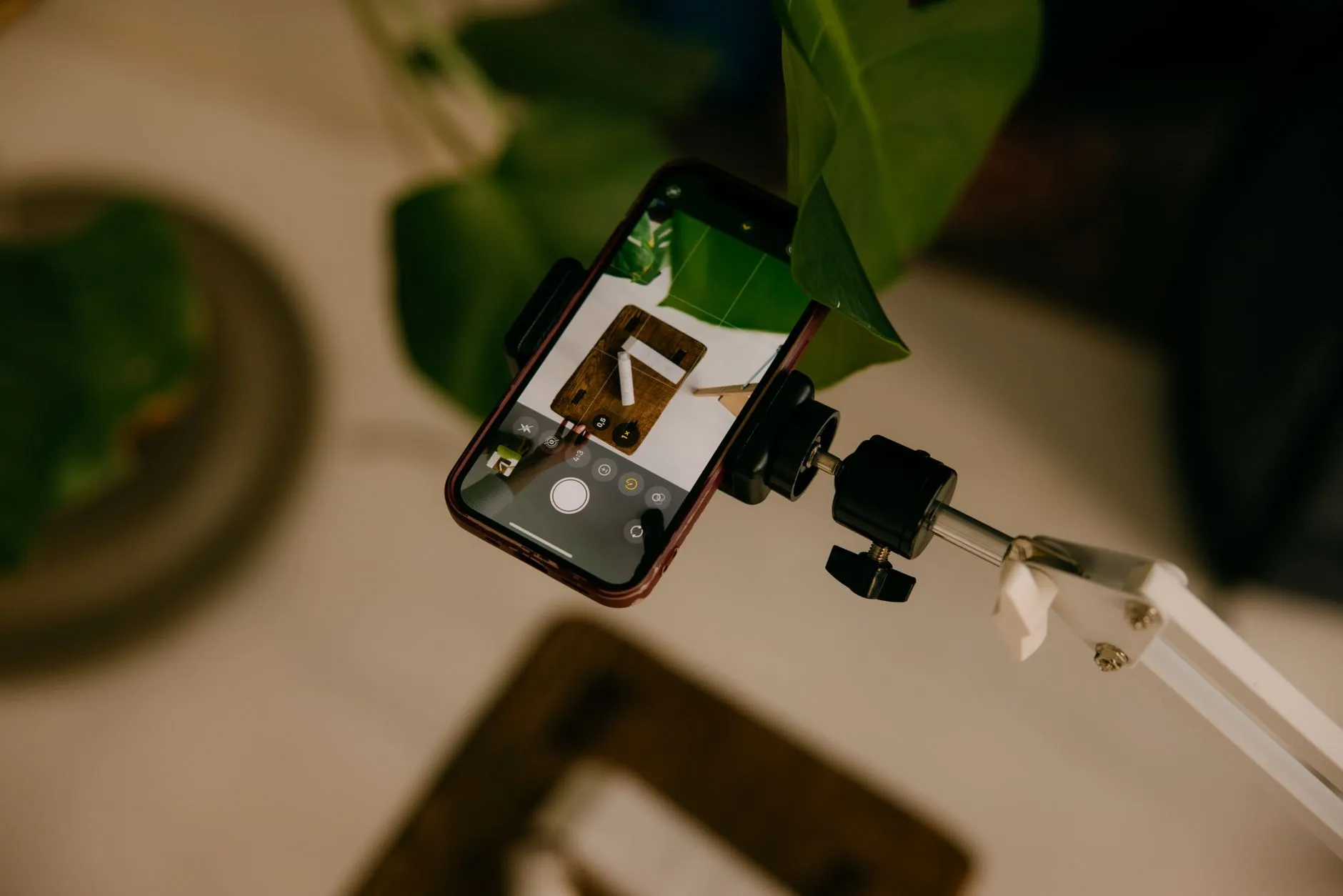 Smartphone on a desk mount filming a styled product flat lay for a social post