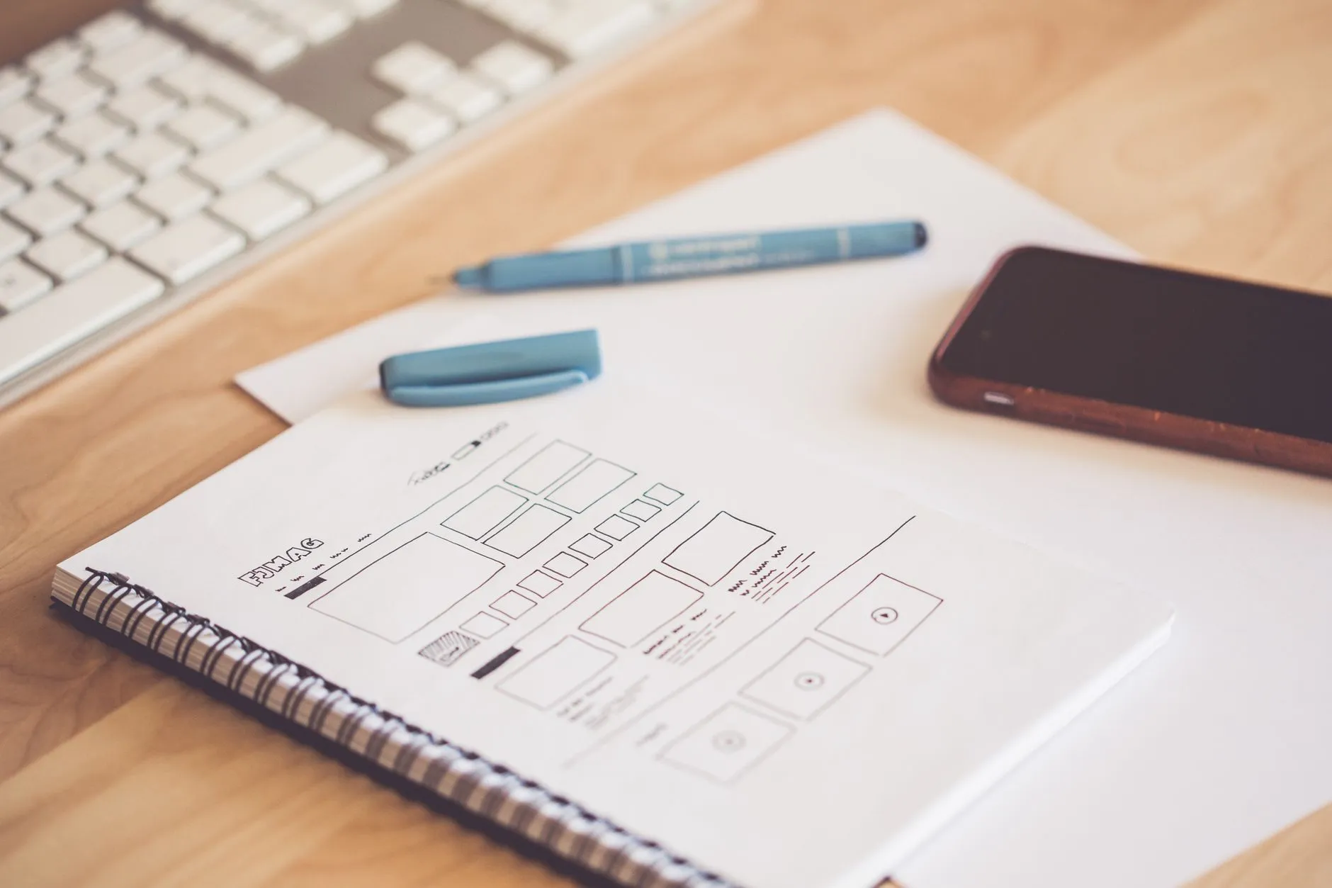 Sketchpad with website wireframes next to a smartphone and keyboard, an early step for a web design company